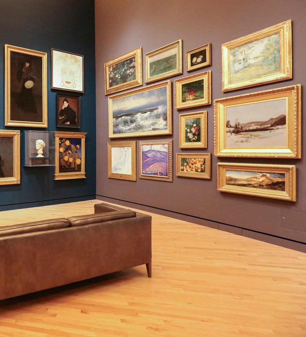A collector's salon wall hung with framed works above a leather sofa